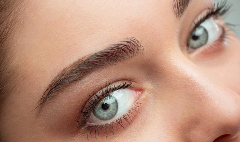 Naheaufnahme eines Gesichts mit betonten Augenbrauen und strahlend blauen Augen.