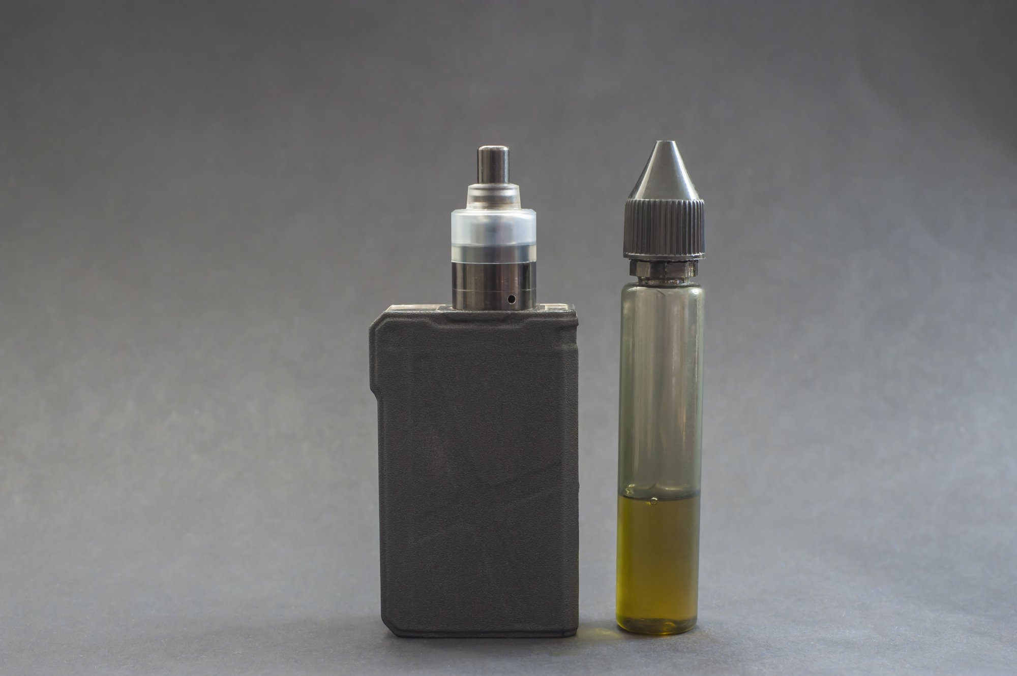 Ein Verdampfergerät links, daneben eine Flasche mit E-Liquid in einer transparenten Verpackung.