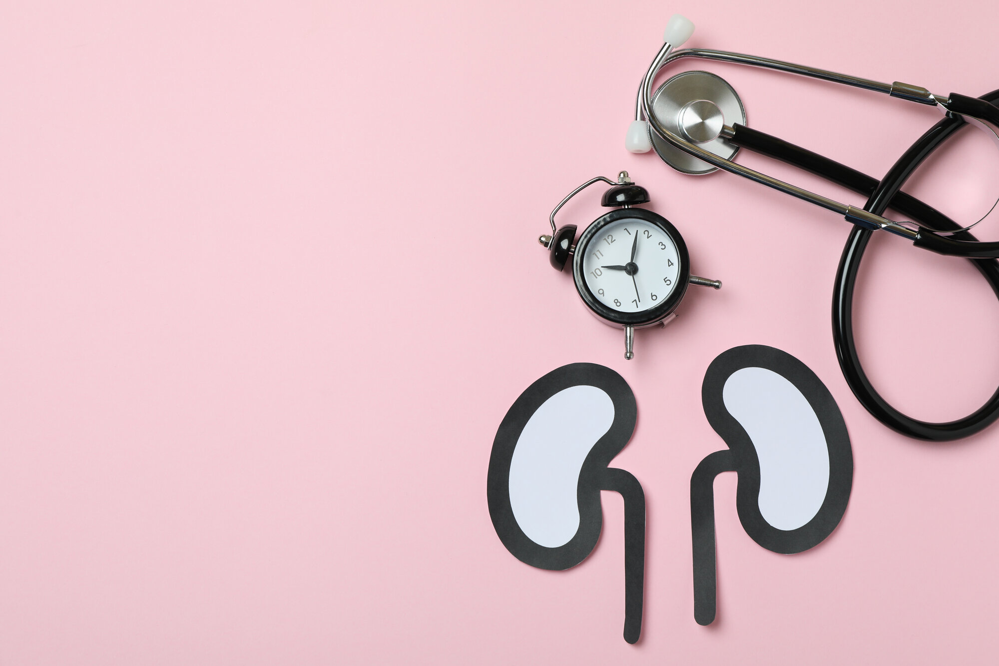 Papierfiguren von Nieren auf einem rosa Hintergrund, daneben eine Armbanduhr und ein Stethoskop.